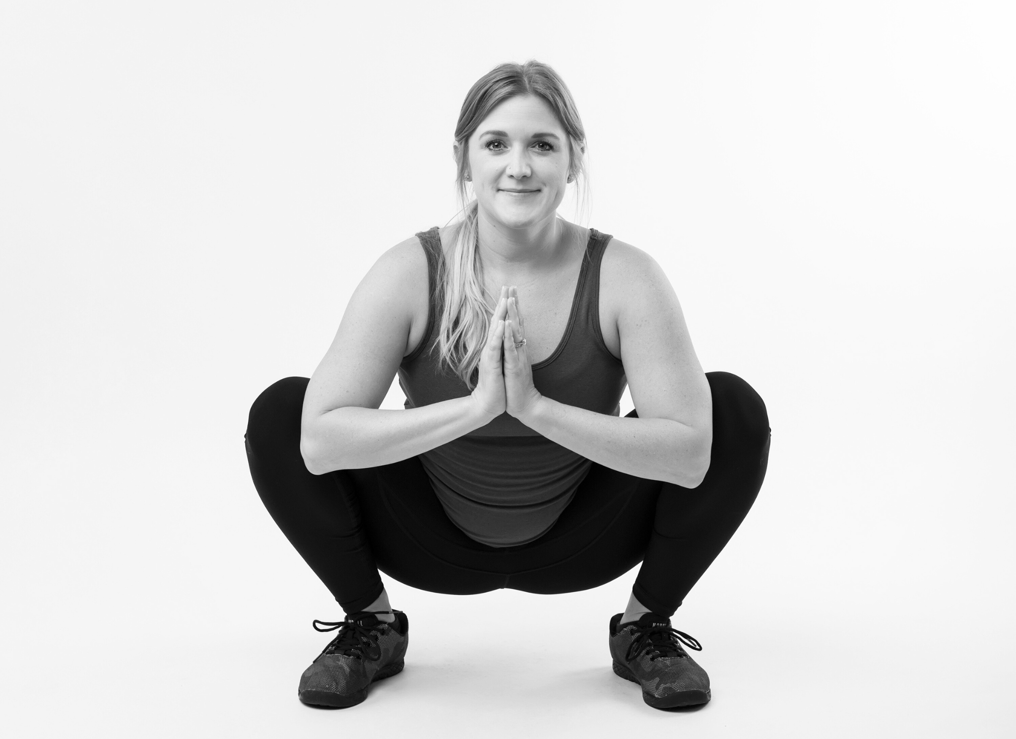 woman sits in deep squat with her hands together in prayer