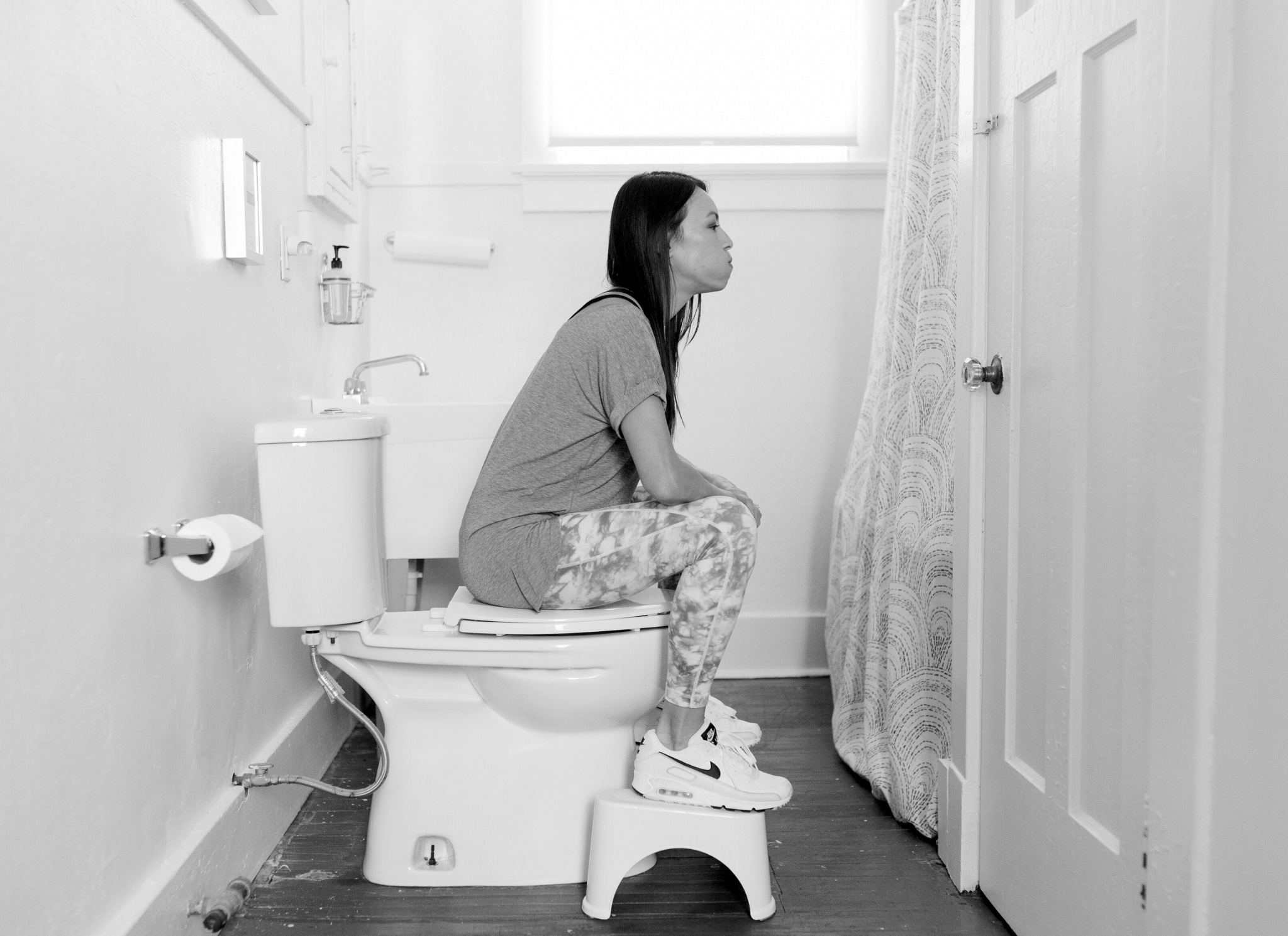 woman sitting on toilet with her feet on a stool