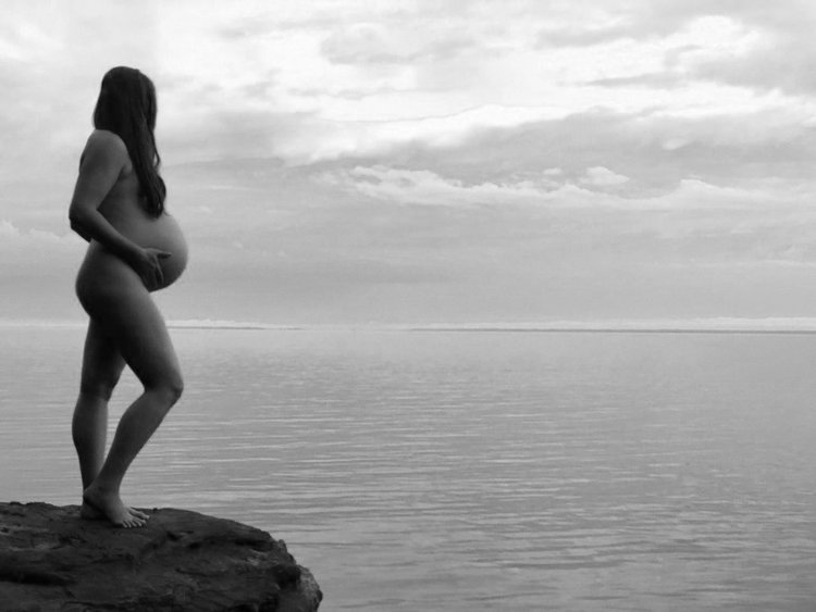 naked pregnant woman overlooking ocean