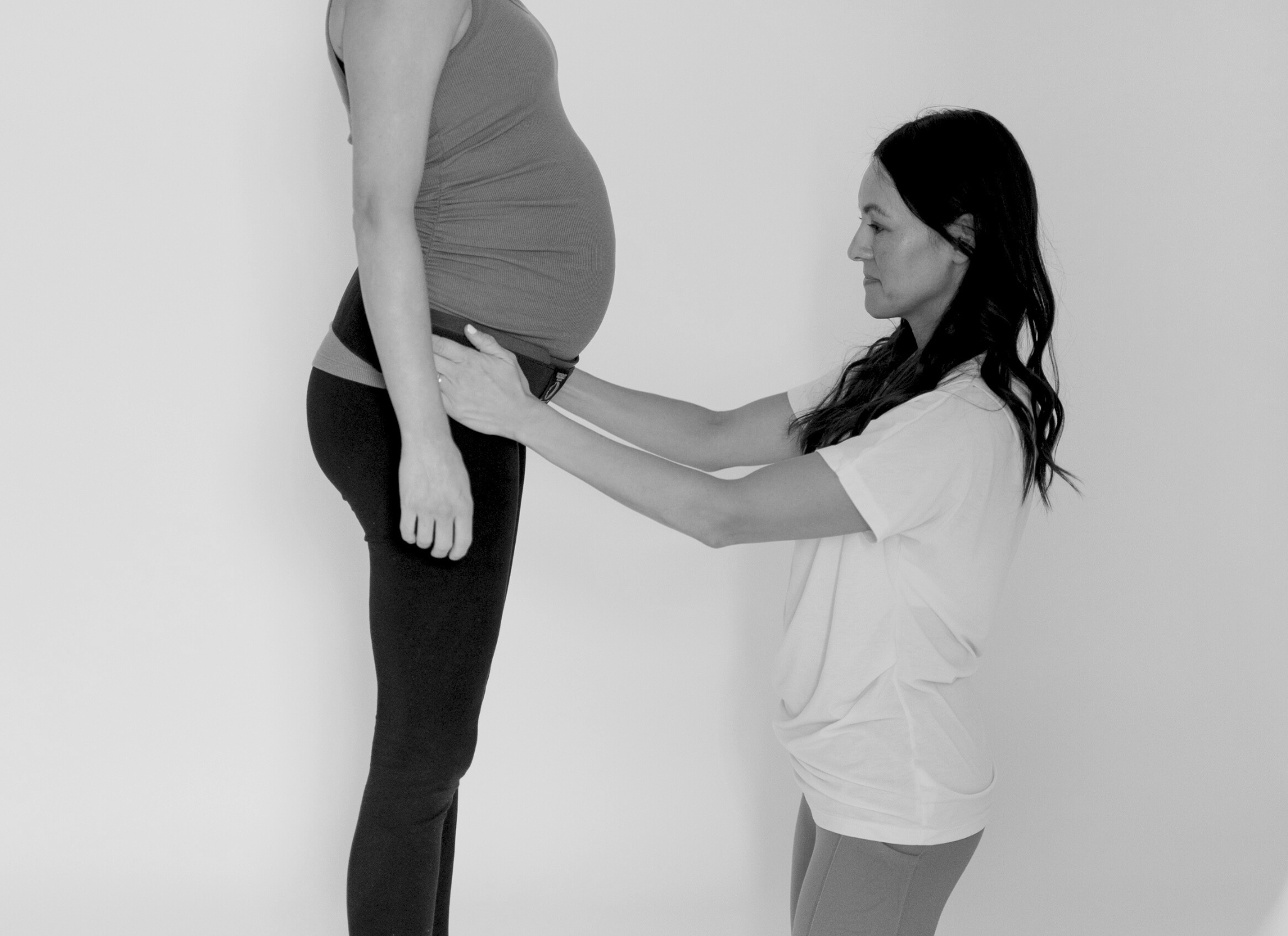 pregnant woman stands in front of a PT while the PT fits her for a serola belt