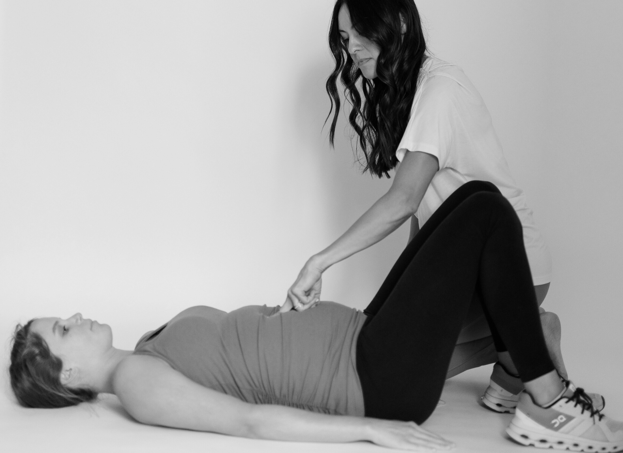 Pregnant woman lays on ground, physical therapist kneels next to her and checks her abdomen for diastasis recti