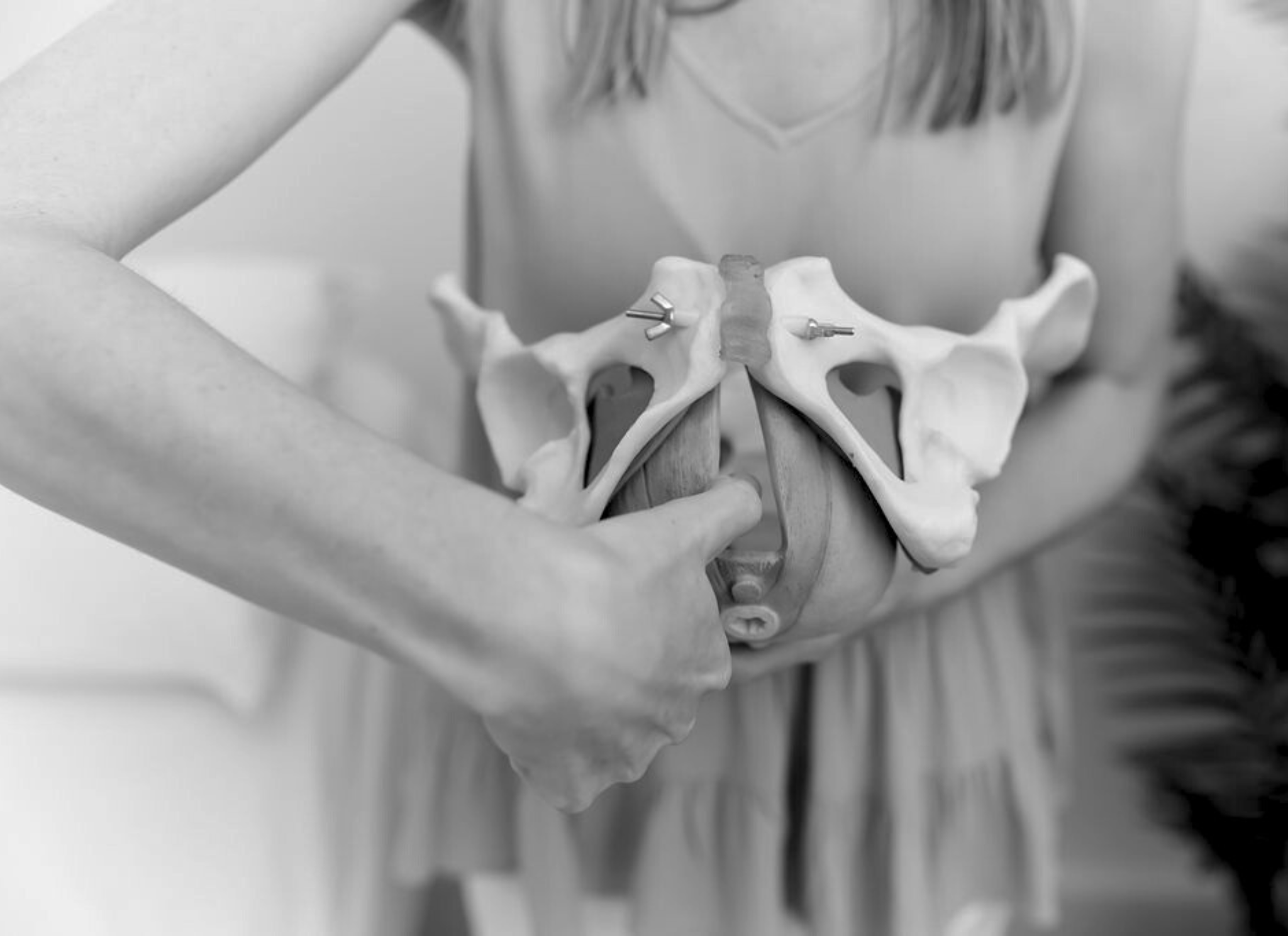 Woman holds model of pelvis, demonstrates perineal massage with her thumb