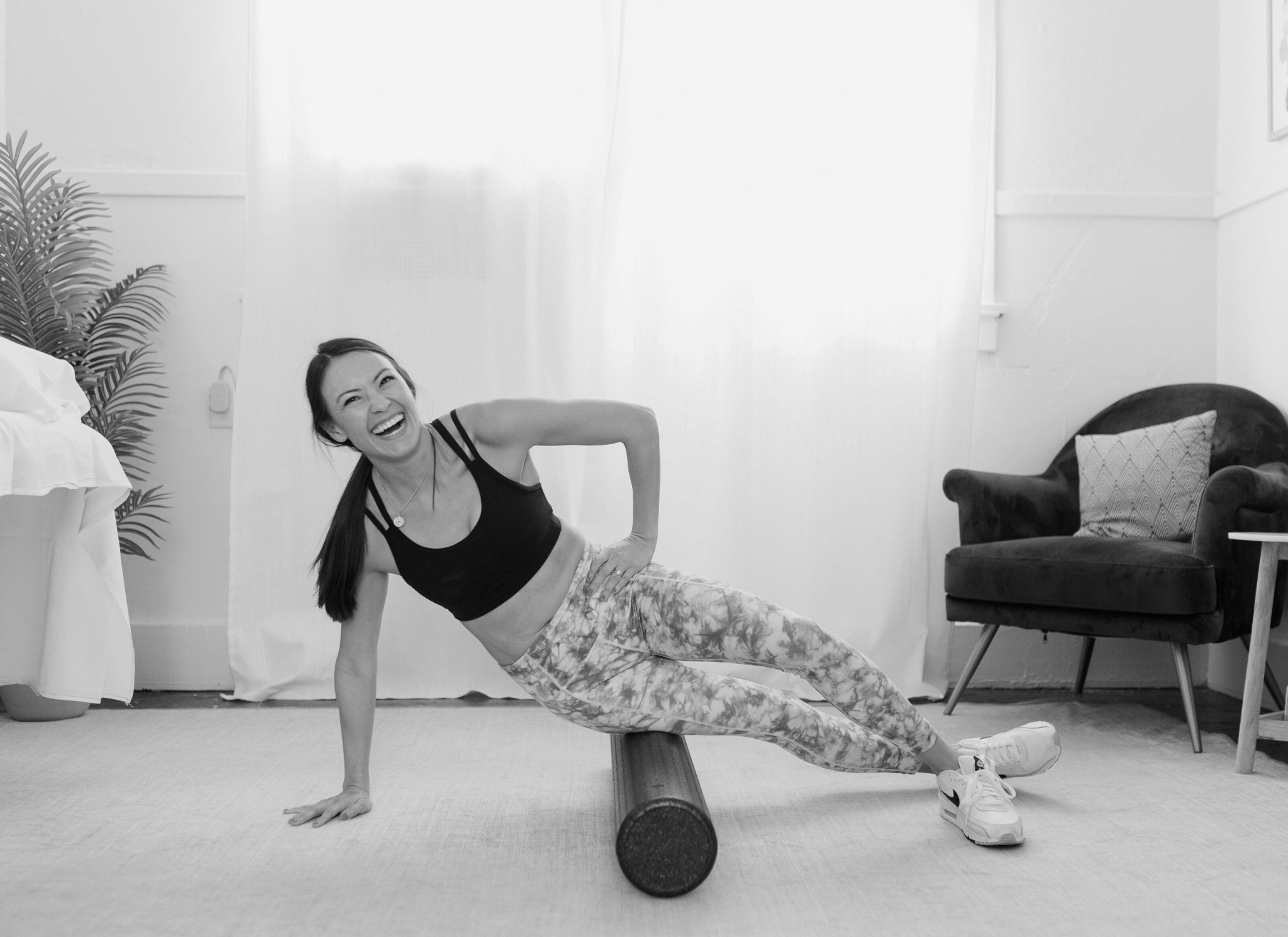 woman lays with hip on foam roller and looks into the camera laughing