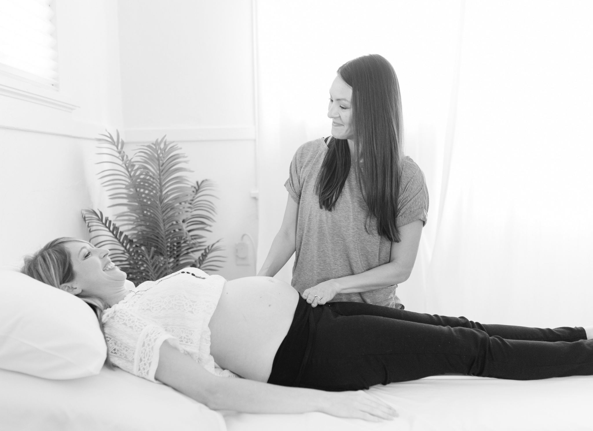 pregnant patient lays on bed with therapist standing over her talking