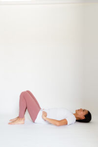 Woman lays on back, her knees are bent, her hands are on her hips.