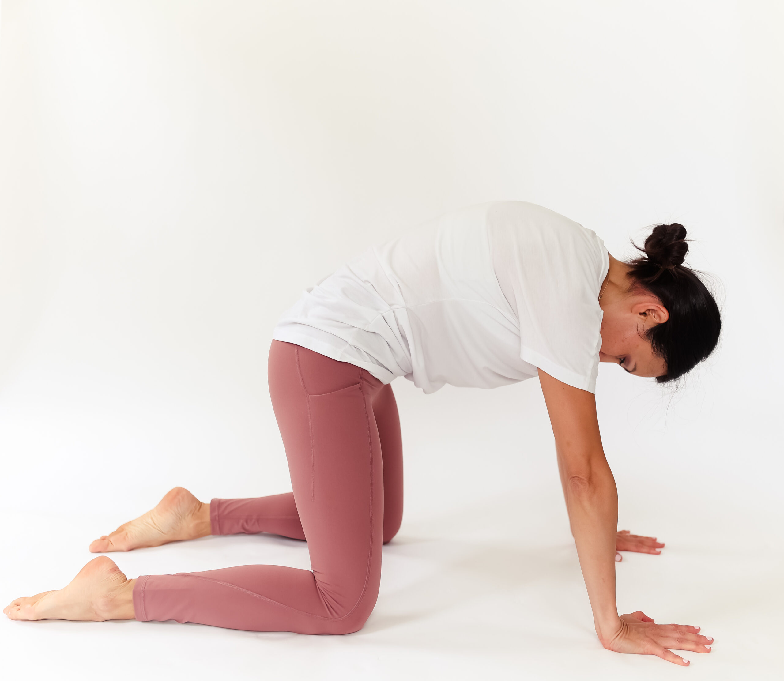 Woman on her hands and knees arches her back in cat cow pose