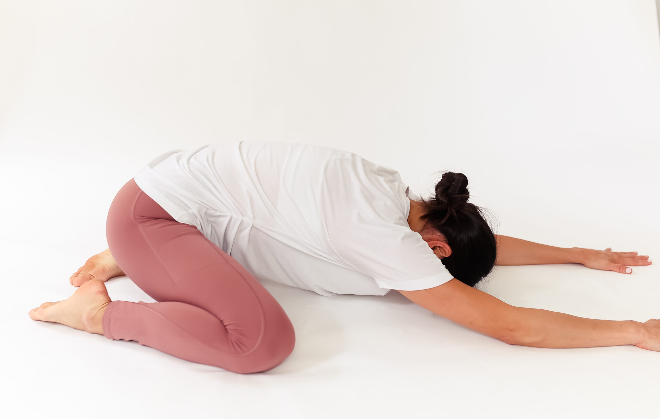 Woman crouches on ground with hands out in front of her, laying down in child's pose for fertility exercise