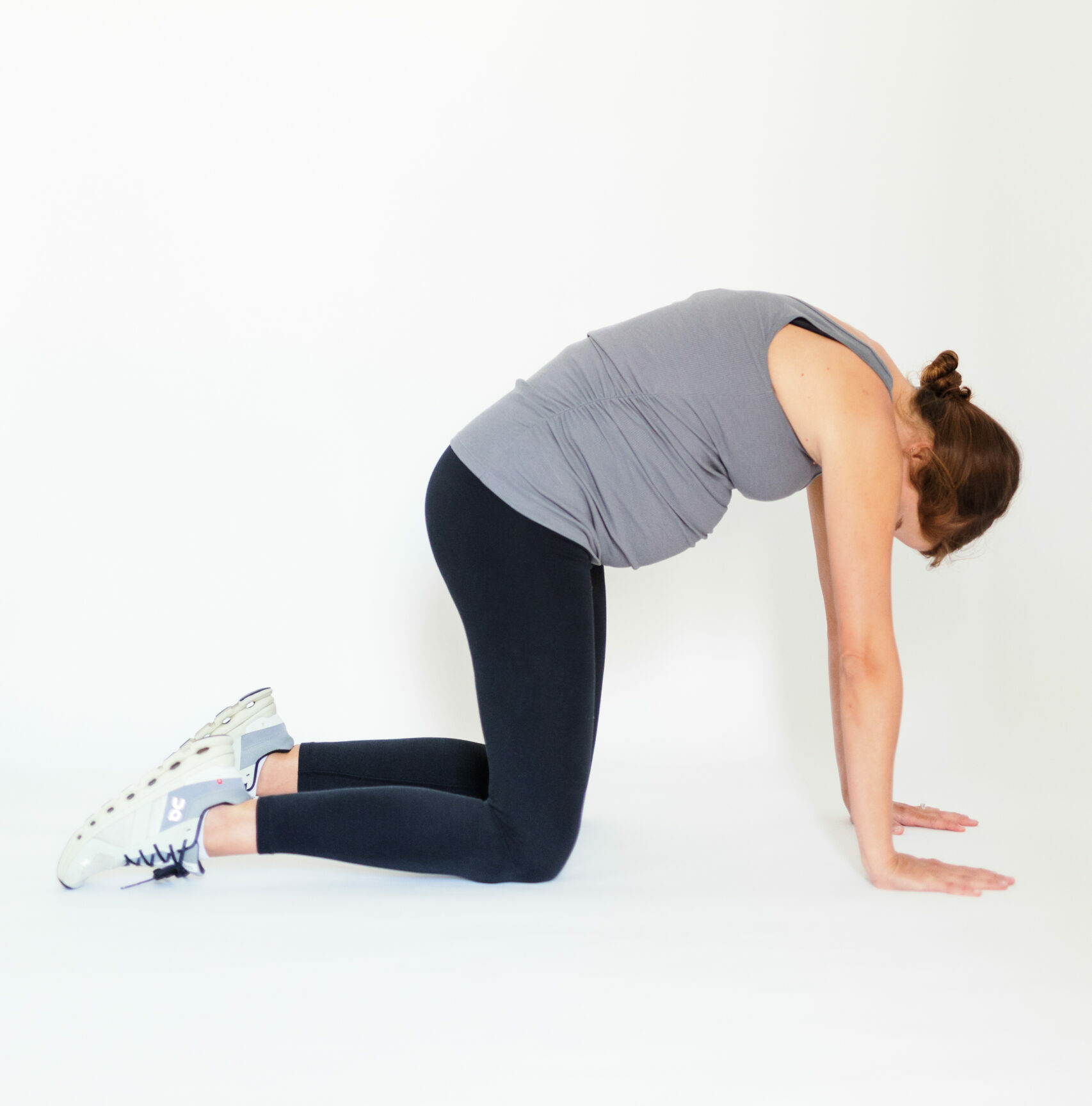 Pregnant woman on hands and knees arches back up and looks down in cat cow pose.