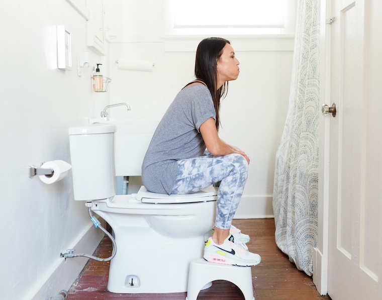 woman sitting on the toilet with feet on squatty potty breathing