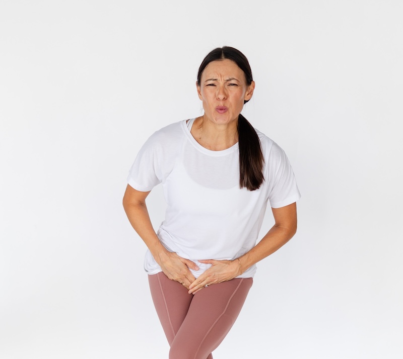woman with a white shirt and pink leggings crossing her legs looking like she has to pee